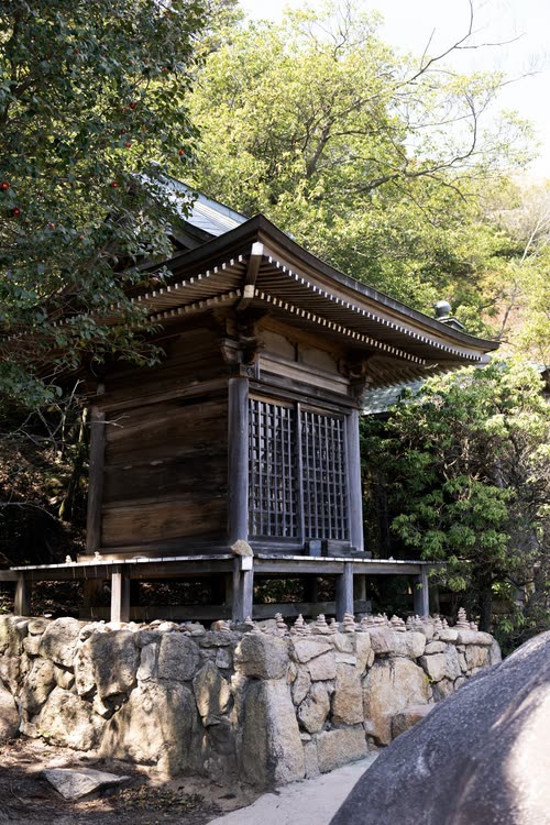 A small timber shrine standing on a stone retaining wall in the forest