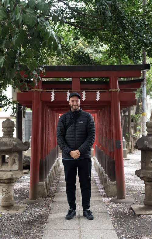 Jordy Scott standing beneath a vermilion torii gate on a stone shrine path