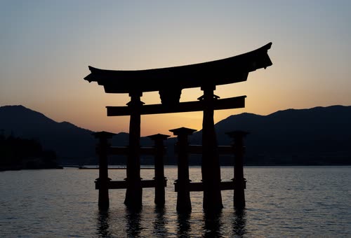 The floating torii gate of Itsukushima silhouetted against a sunset sky