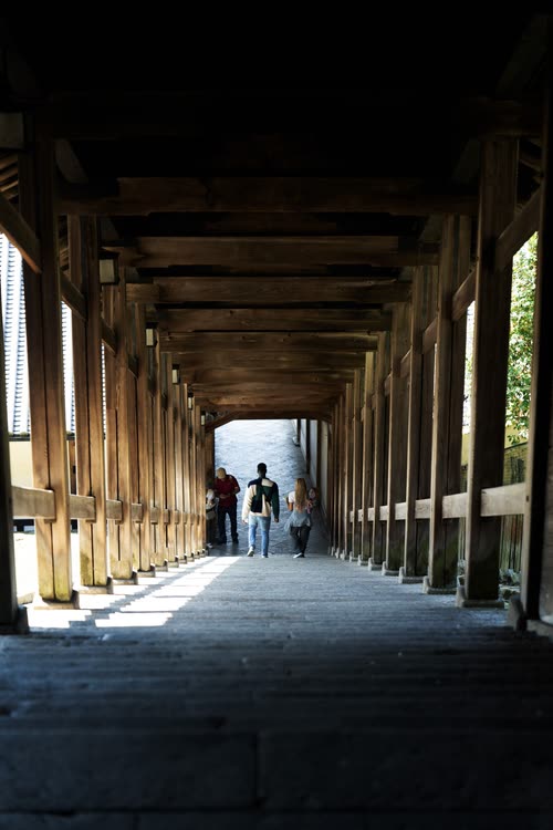 Visitors walking a long timber colonnade beside a temple hall