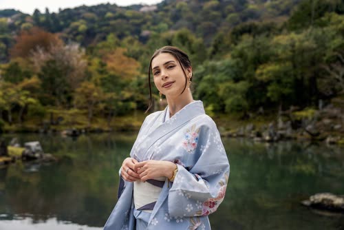 A woman in a pale floral kimono beside a Japanese garden pond in Kyoto