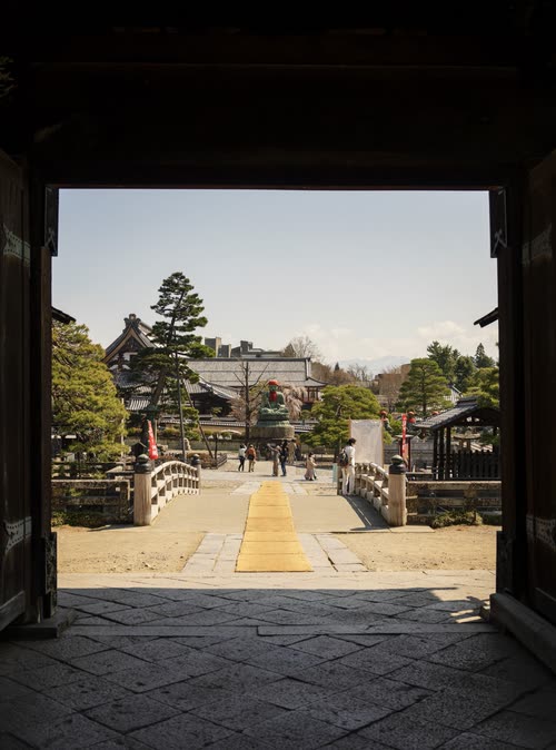 A stone bridge and temple grounds framed through a dark timber gateway