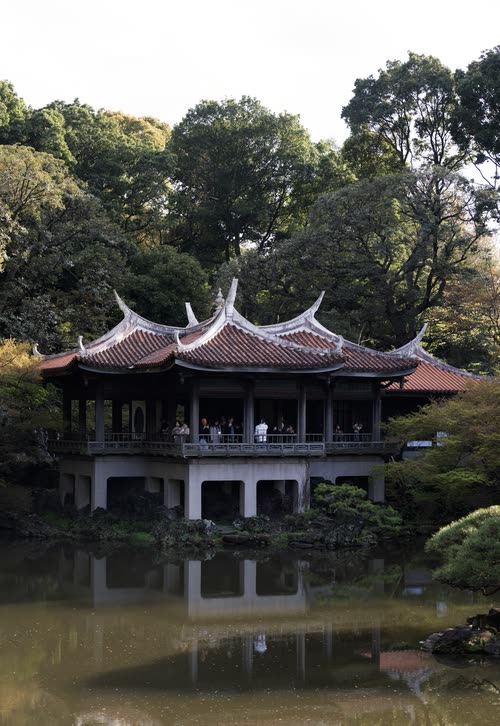 An ornate pavilion with sweeping tiled roofs reflected in a still garden pond