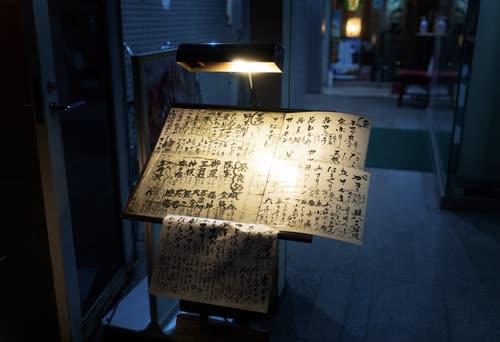 A handwritten calligraphy menu lit by a single lamp outside a restaurant