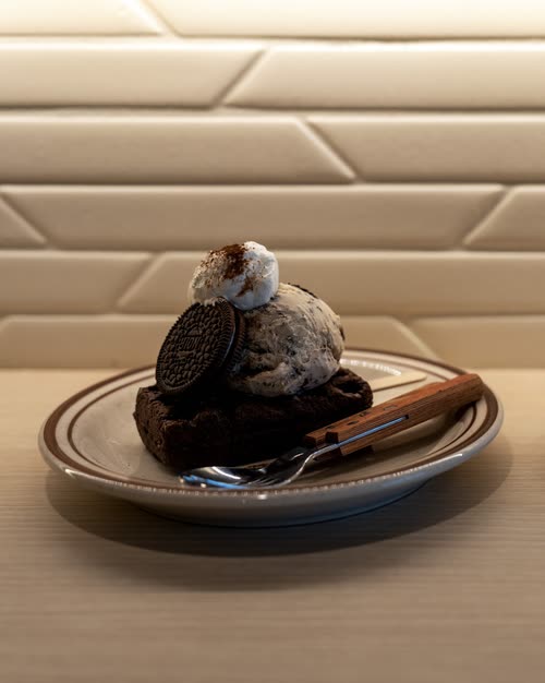 A dessert of brownie, cream and biscuit plated on a ceramic dish