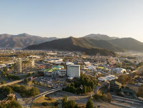 Aerial view of a Japanese town and ferris wheel below sunlit mountains