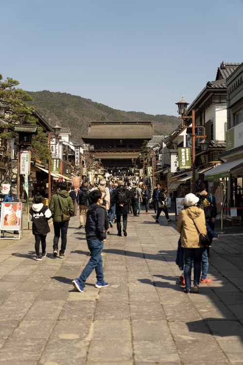 Visitors walking the flagstone approach to a temple gate between old shopfronts