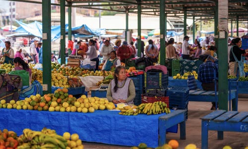 A vendor behind stacked fruit at a covered market in the Sacred Valley