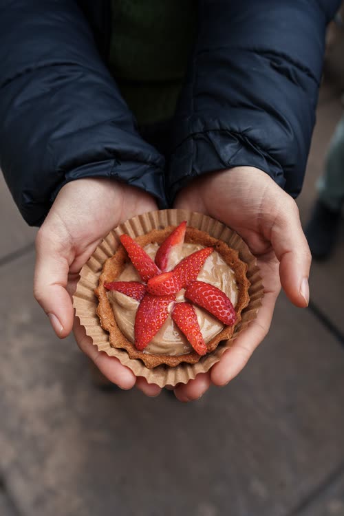 Hands holding a small strawberry tart in a paper case