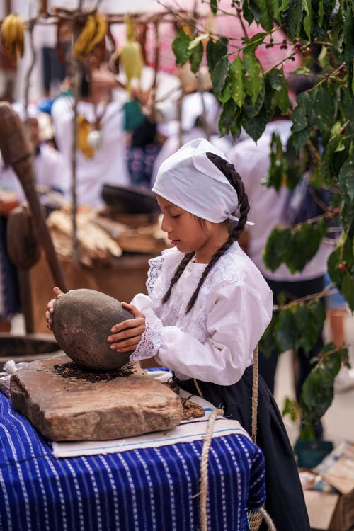 A girl in traditional dress grinding grain with a stone at a market demonstration
