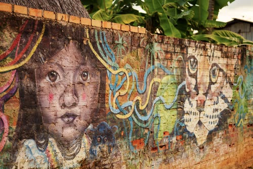 A painted mural of a child's face on a brick wall beneath banana palms
