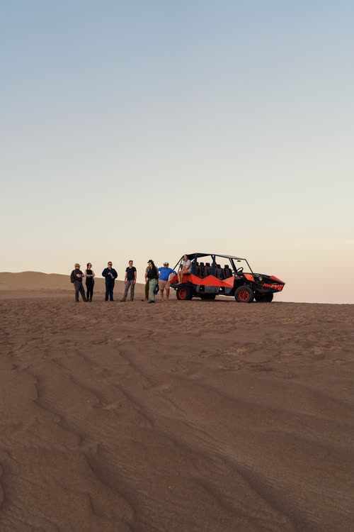 A tour group standing beside their dune buggy on the open desert