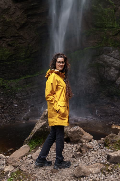 A woman in a yellow raincoat at the base of a tall waterfall in Peru