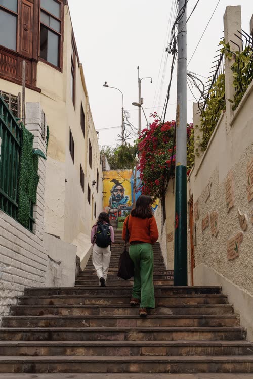 Two people climbing a narrow flight of steps between painted walls