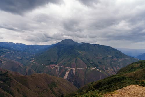 A road winding across steep green Andean ridges under heavy cloud