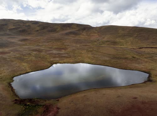 A still lagoon reflecting cloud on the open high-altitude puna grassland