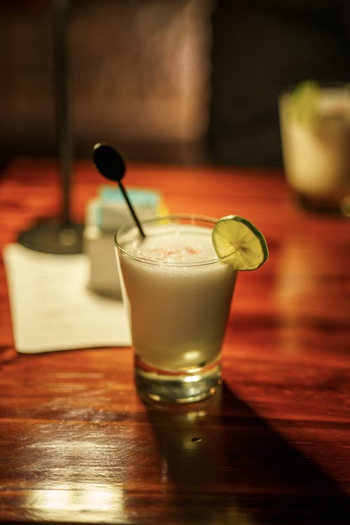 A pisco sour with a lime slice on a wooden bar top