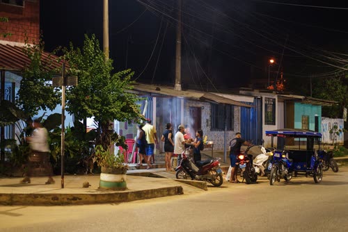 Neighbours and motorbikes gathered on a street corner at dusk in a Peruvian town