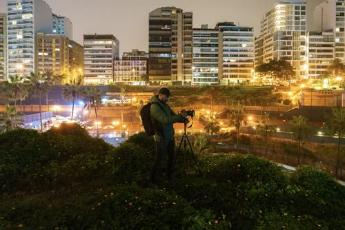 A photographer working on a tripod above the lit high-rises of Miraflores, Lima