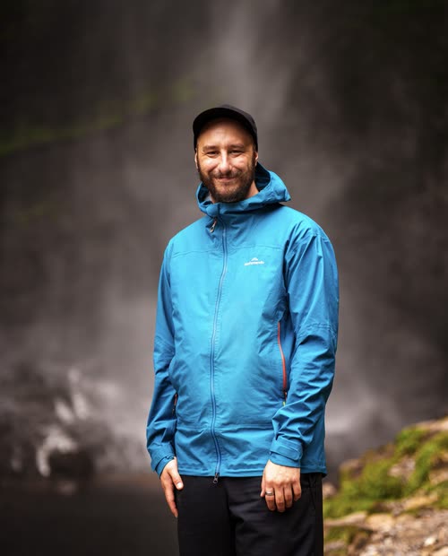 Jordy Scott in a blue rain jacket in front of the spray of Gocta Falls
