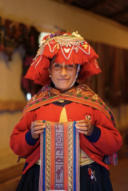 A Quechua woman in traditional red dress holding a handwoven textile band