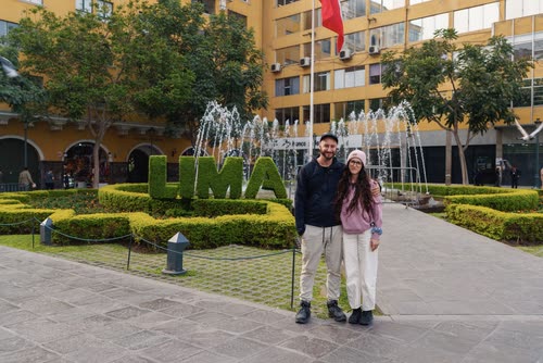 A couple standing by the hedged LIMA sign in front of a fountain