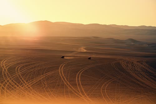 The sun setting over buggy tracks scored across the Huacachina dunes