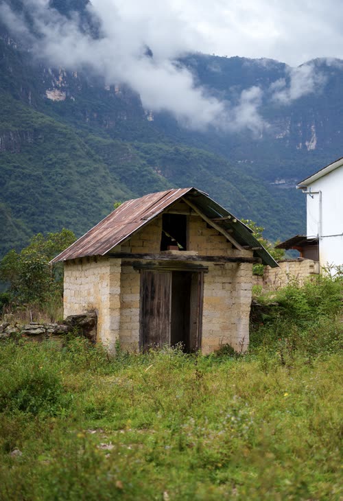 A weathered adobe hut standing below cloud-wrapped Andean cliffs