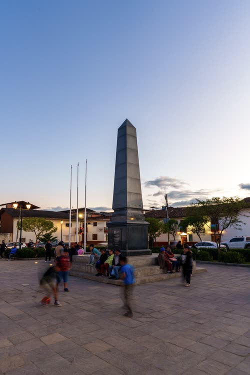 An obelisk monument on a town plaza at sunset with families gathered below
