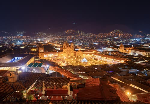 The lit Plaza de Armas and tiled rooftops of Cusco seen from above at night