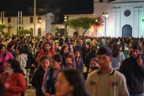 A crowd filling a town square in front of a white colonial church at night