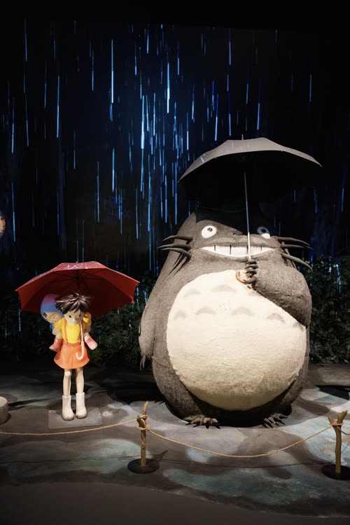 A Totoro figure holding an umbrella in the rain in a Studio Ghibli exhibition set
