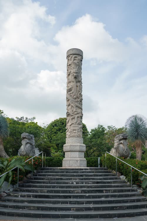A carved stone memorial column flanked by lion statues at the top of a stairway, Singapore