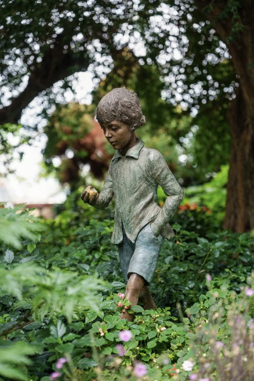 A bronze statue of a boy running through a planted garden bed, Singapore
