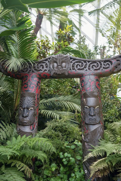 A carved wooden gateway with two figures set among tree ferns, Singapore