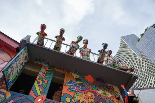 Painted figures lining the roof of a brightly muralled building in Singapore
