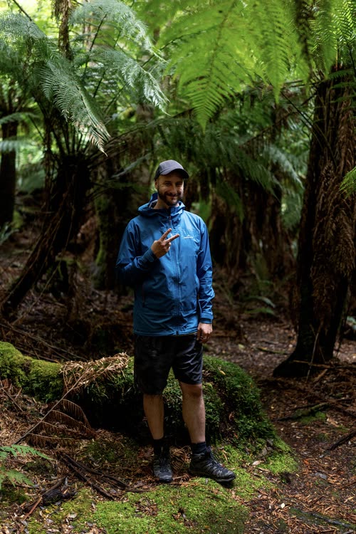 Jordy Scott in a blue rain jacket among tree ferns in Tasmanian rainforest