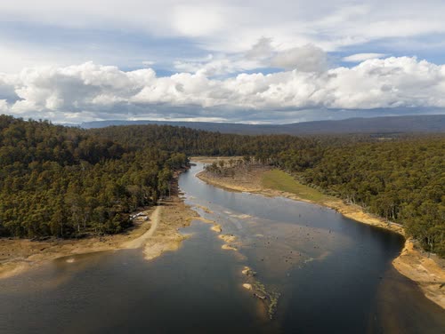 Aerial view of a river winding through bush toward distant ranges, Tasmania