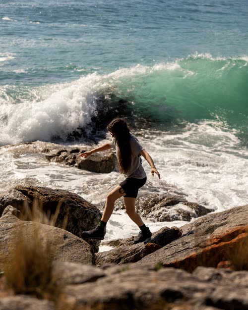 A woman on the rocks as a wave breaks behind her, Tasmania