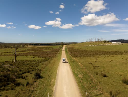 A campervan on a straight gravel road through Tasmanian farmland
