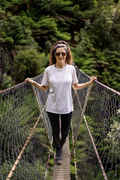 A woman crossing a swing bridge through tree ferns in Tasmania