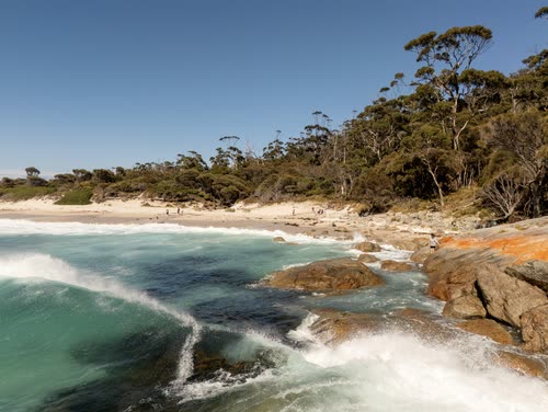 Aerial view of surf breaking over orange lichen boulders at the Bay of Fires, Tasmania