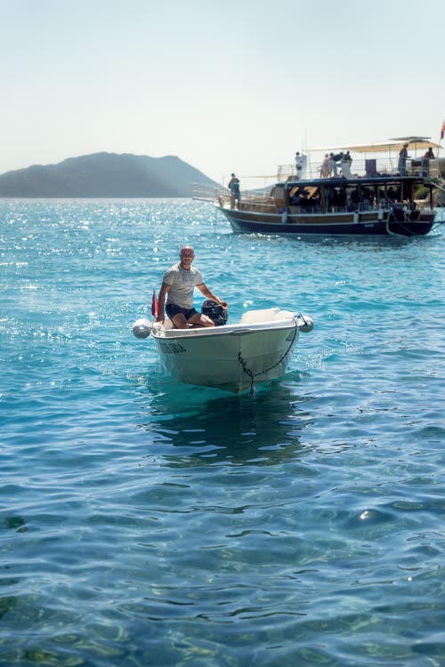 A man in a small boat on clear turquoise water beside a gulet, Turkey