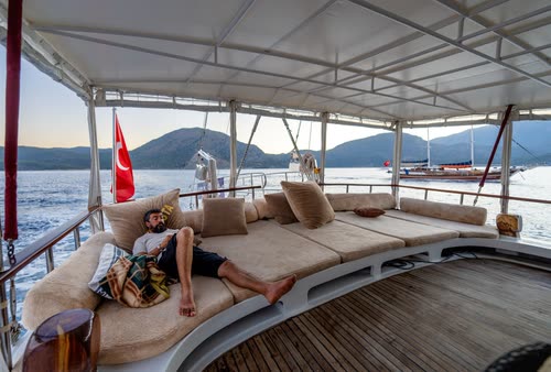 A man resting on the shaded deck cushions of a gulet, Turkey