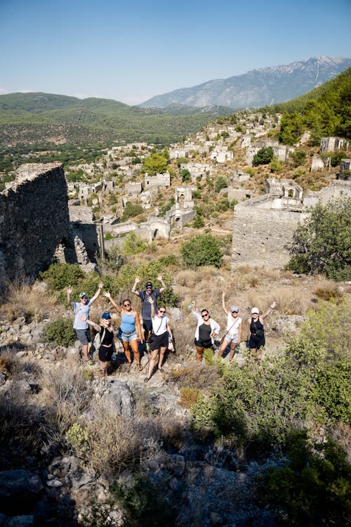 A tour group with arms raised among the ruins of Kayakoy, Turkey