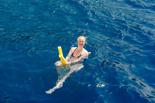 A woman swimming with a pool noodle in clear blue water, Turkey