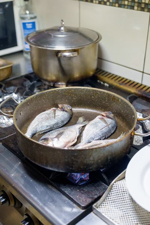 Whole fish frying in a pan on a boat galley stove, Turkey