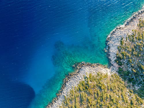 Aerial view of a rocky shoreline where turquoise shallows meet deep blue, Turkey