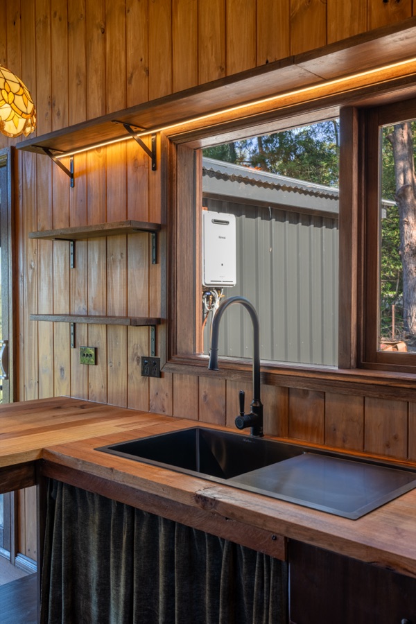 A black tap and undermount sink on a timber benchtop beneath a picture window