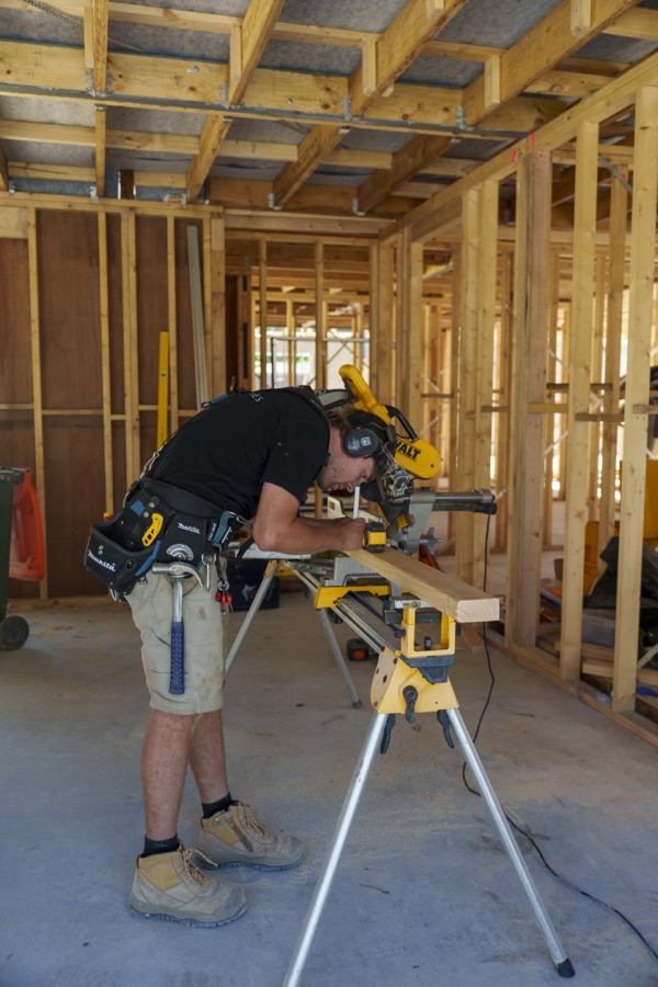A carpenter cutting timber on a drop saw inside the frame